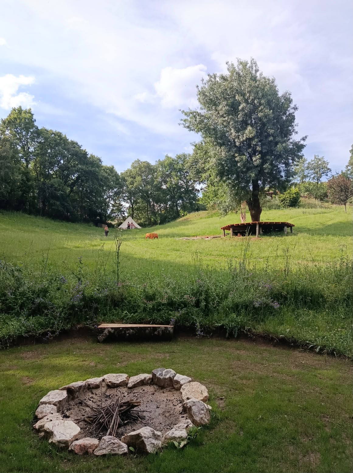 Stone firepit in the meadow, willow and bell tent beyond